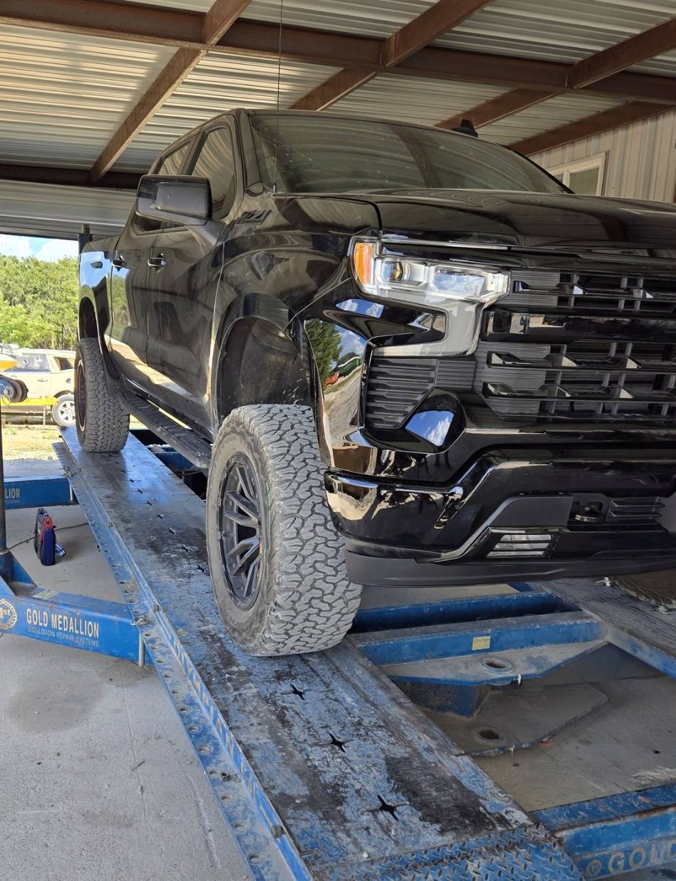 A pickup with its front bumper and grille removed, standing up on the shop's rack.