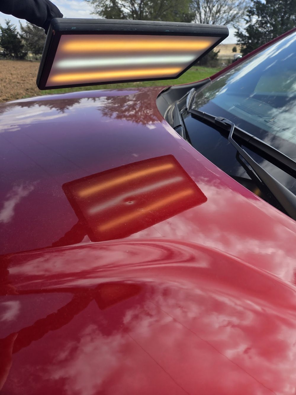 An infrared curing lamp glowing above a deep red hood, its bars reflected in the wet looking paint.